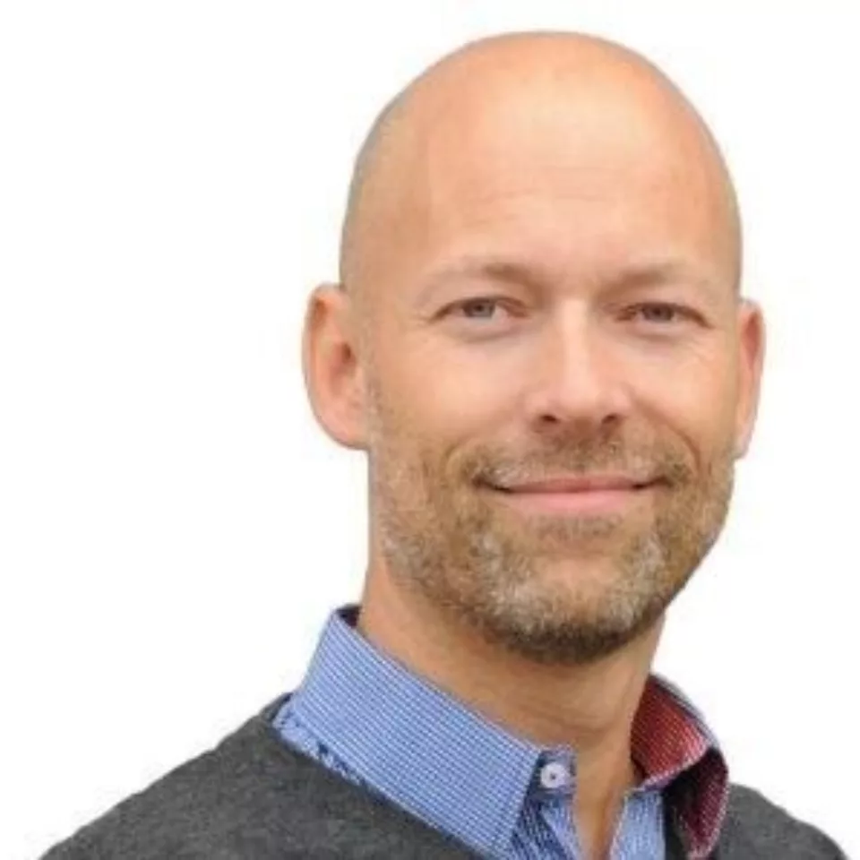 Mann smiler i skjorte og genser